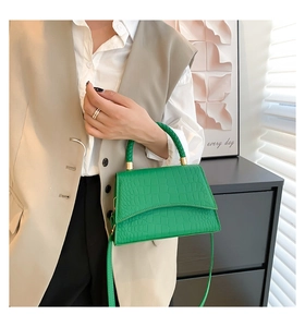 Detail of green crocodile texture handbag with woven handle held by a model