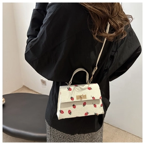 Detailed shot of white corduroy handbag with red strawberry patterns and gold twist lock