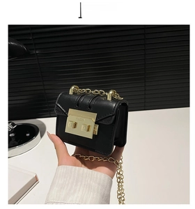 Mini black leather crossbody bag held by hand to show size and golden chain strap