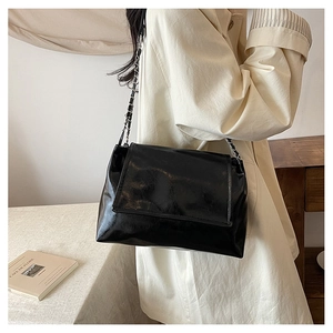 Detail of black glossy patent leather shoulder bag with silver metal chain strap