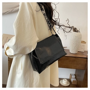 Close-up of black glossy leather shoulder bag with metallic chain strap and flap design