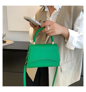 Detail of green crocodile texture handbag with woven handle and gold hardware accents