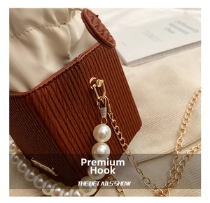 Close-up of pearl handle and gold metal hook on brown pleated leather crossbody bag