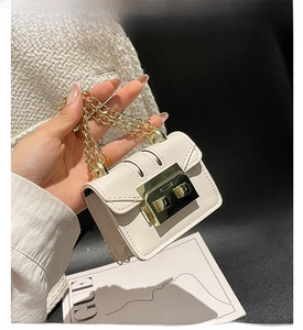 Close-up of white mini square bag with chunky gold chain and metallic push lock detail