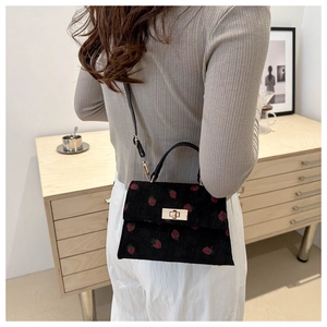 Detail of black corduroy handbag featuring red strawberry print and golden buckle