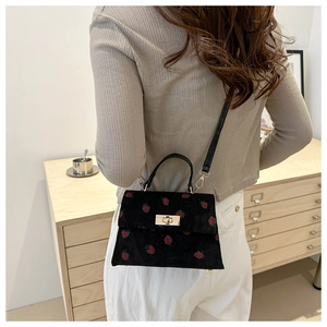 Detail of strawberry embroidery and gold twist lock on black corduroy crossbody bag