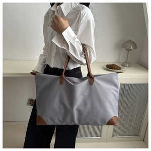Large grey Oxford fabric tote bag with brown leather handles worn by a model in a room