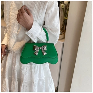Détail d'un sac à main vert avec nœud argenté et bordure inférieure festonnée originale