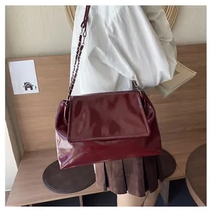 Detail of burgundy patent leather tote bag with glossy finish and silver chain strap