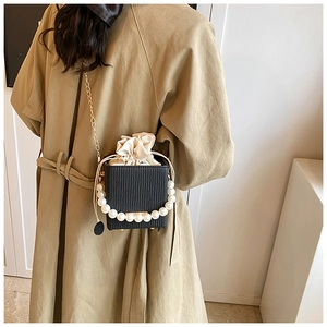 Detail of black pleated box bag with large pearl handle and cream drawstring inner pouch