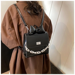 Detail of black patent leather backpack with bow accent and silver chain on brown coat