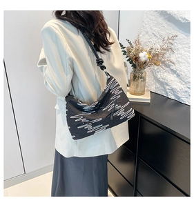 Detail of black shoulder bag with white wavy embroidery and knotted strap design