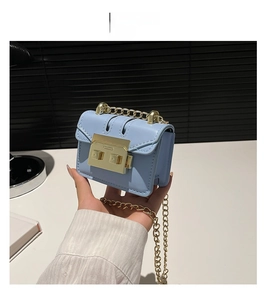 Detail of light blue mini flap bag with gold rectangle clasp and metal chain strap