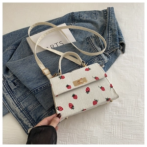 Detail of white corduroy crossbody bag featuring red strawberry print and gold twist lock