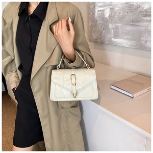 Detail of a creamy white shoulder bag with a gold U-shaped buckle and textured flap