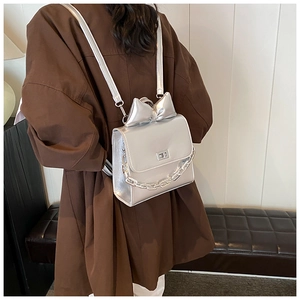 Silver metallic backpack with a large bow detail and chain strap worn by a model