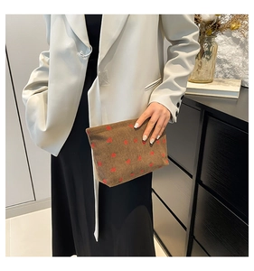 Brown corduroy clutch bag with red strawberry pattern held against a white blazer
