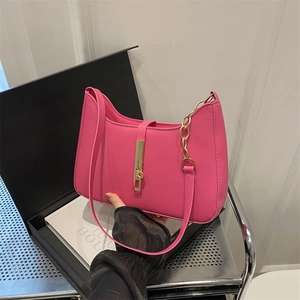 Sac bandoulière rose fuchsia avec chaîne dorée et fermoir devant une boîte cadeau
