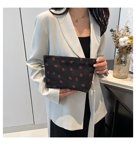 Detail of black corduroy clutch bag with red strawberry embroidery held by a model