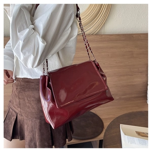 Close-up of wine red patent leather tote bag with silver chain strap and magnetic flap