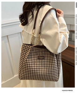 Detailed view of houndstooth tote bag featuring gold chain strap and premium leather trim