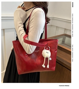 Detail of red leather tote bag featuring sleek shoulder straps and a plush doll charm