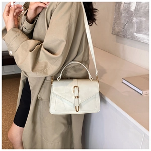 Detail of creamy white crossbody bag with gold horseshoe buckle and geometric stitching