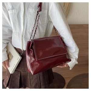 Side view of a burgundy chain tote bag in glossy patent leather on a shoulder