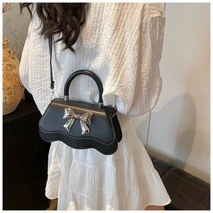 Détail du nœud en métal argenté sur sac noir avec une robe blanche plissée