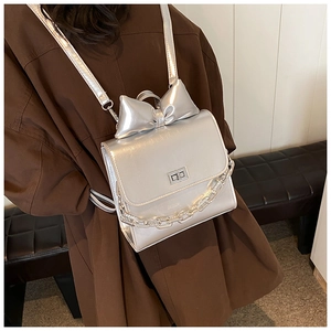 Detail of silver metallic backpack featuring a large bow and chunky chain strap