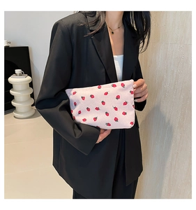 Close-up of strawberry print corduroy clutch held by a model in a black blazer