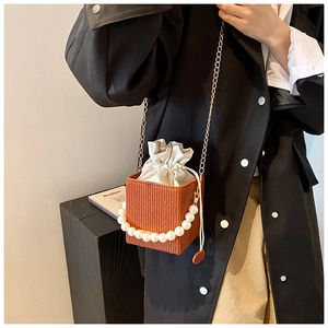 Detail of a brown pleated crossbody bag with pearl handle and golden chain on a model