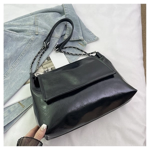 Close-up of glossy black tote bag featuring metallic chain strap on white fabric