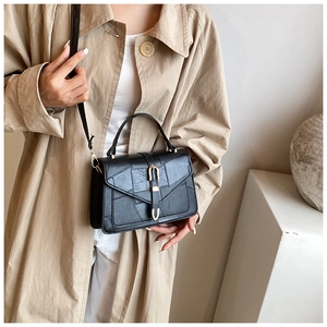 Detail of black textured leather crossbody bag with gold U-shaped buckle and top handle