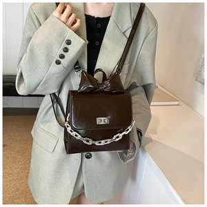 Detail of dark brown glossy leather crossbody bag with silver chain and bow accent