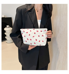 Close-up of corduroy tote bag with strawberry prints held by a model in a black blazer