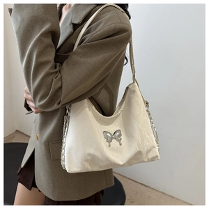Detail of cream shoulder bag with silver butterfly emblem and metal chain strap on a model