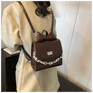 Detail of a dark brown glossy backpack with bow, silver chain, and twist lock on a model