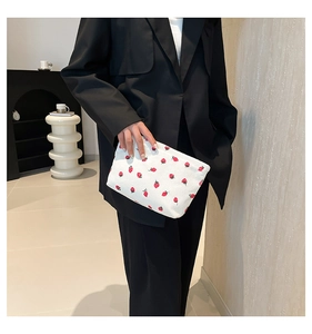 Detail of corduroy makeup bag with strawberry print held by a model in minimalist setting