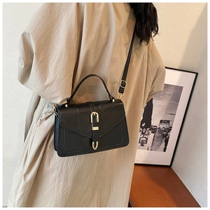 Detail of a vintage black leather crossbody bag with a gold U-shaped buckle on a beige coat