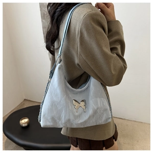 Detail of light blue pleated shoulder bag with metal butterfly and chain strap on model