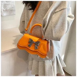 Détail du sac bandoulière orange avec grand nœud en métal argenté et bordure ondulée