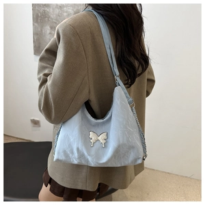 Detail of light blue textured shoulder bag with pearl butterfly buckle on model