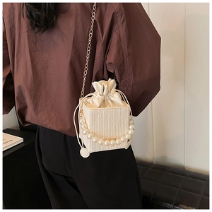 Detail of cream crossbody bag featuring faux pearl handle and gold chain strap on model