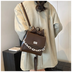 Detail of dark brown patent leather crossbody bag with bow decoration and silver chain