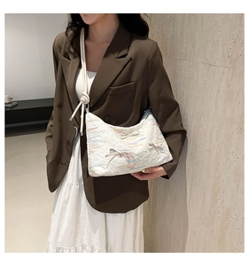 Detail of white tote bag with quilted texture, silk bow, and colorful embroidery accents