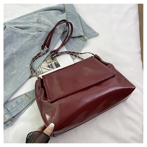 Detailed macro view of glossy burgundy patent leather bag with silver chain strap
