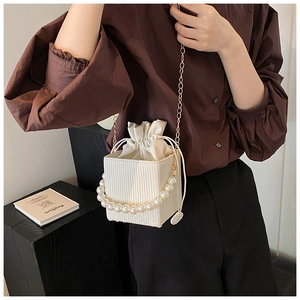 Detail of white pleated bucket bag with pearl handle and golden chain shoulder strap