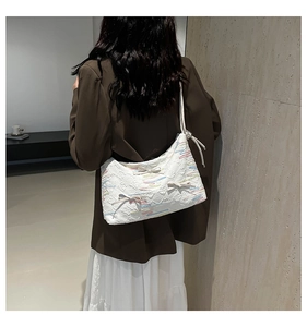 Detail of white shoulder bag with textured fabric, bow accents, and colorful embroidery