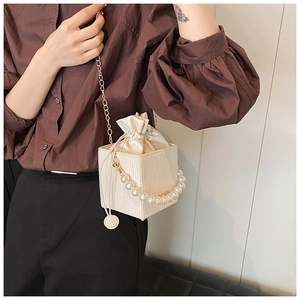 Detail of white pleated bucket bag with gold chain strap and pearl handle on model